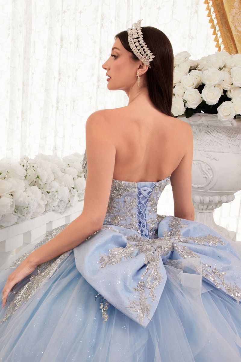 A woman in the Ladivine Strapless Quinceanera Dress 15715, a blue ball gown featuring elegant bow detail.